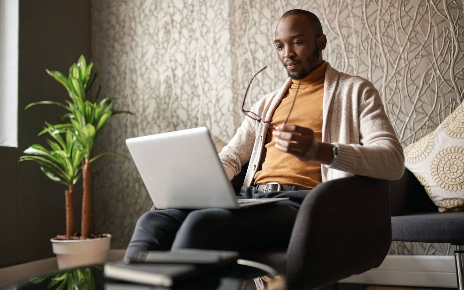 A man in an armchair holding laptop and glasses