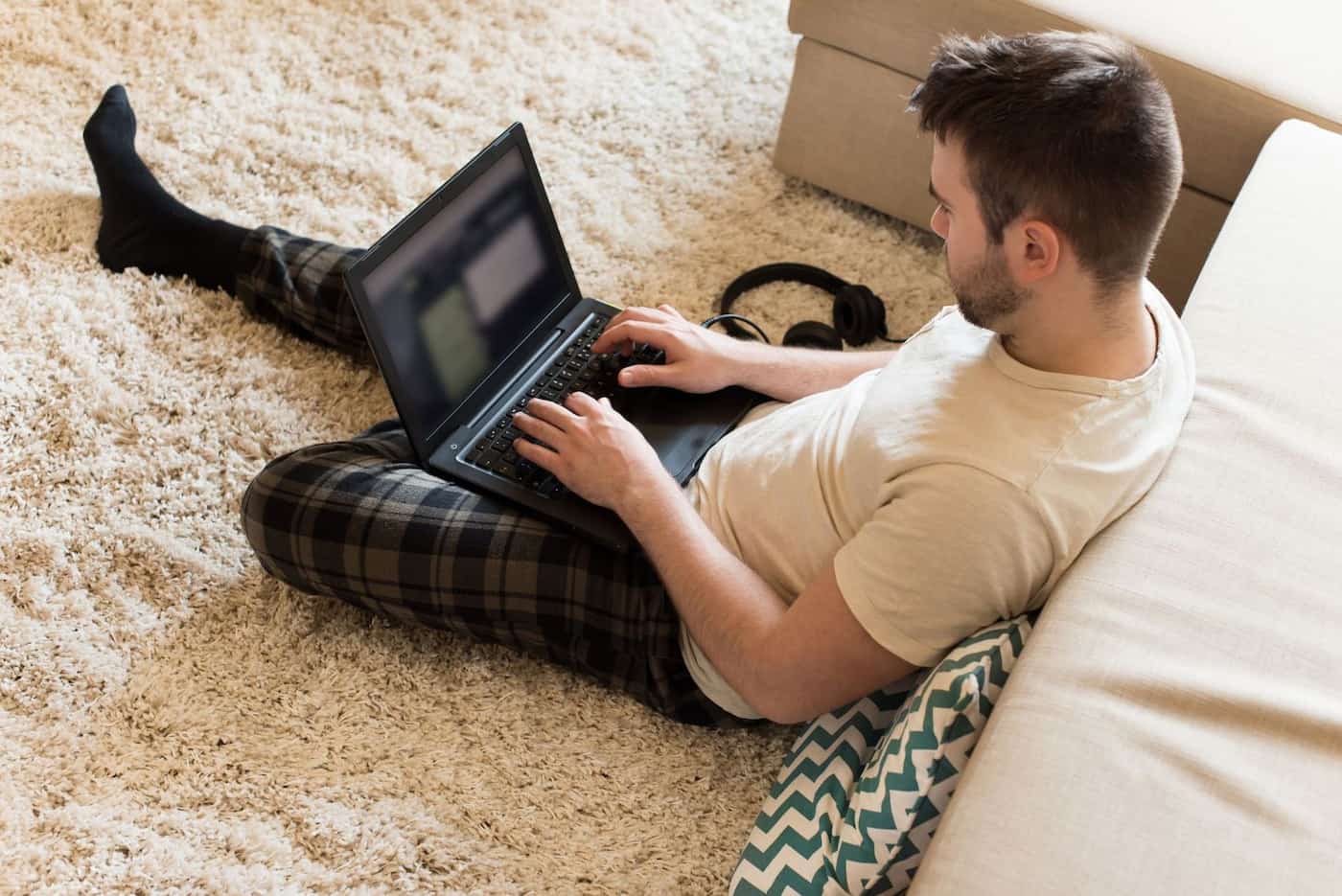 A mn typing on laptop on the floor in the living room